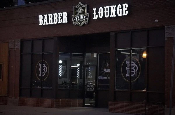 Nighttime exterior of Prime Barber Lounge with illuminated storefront sign
