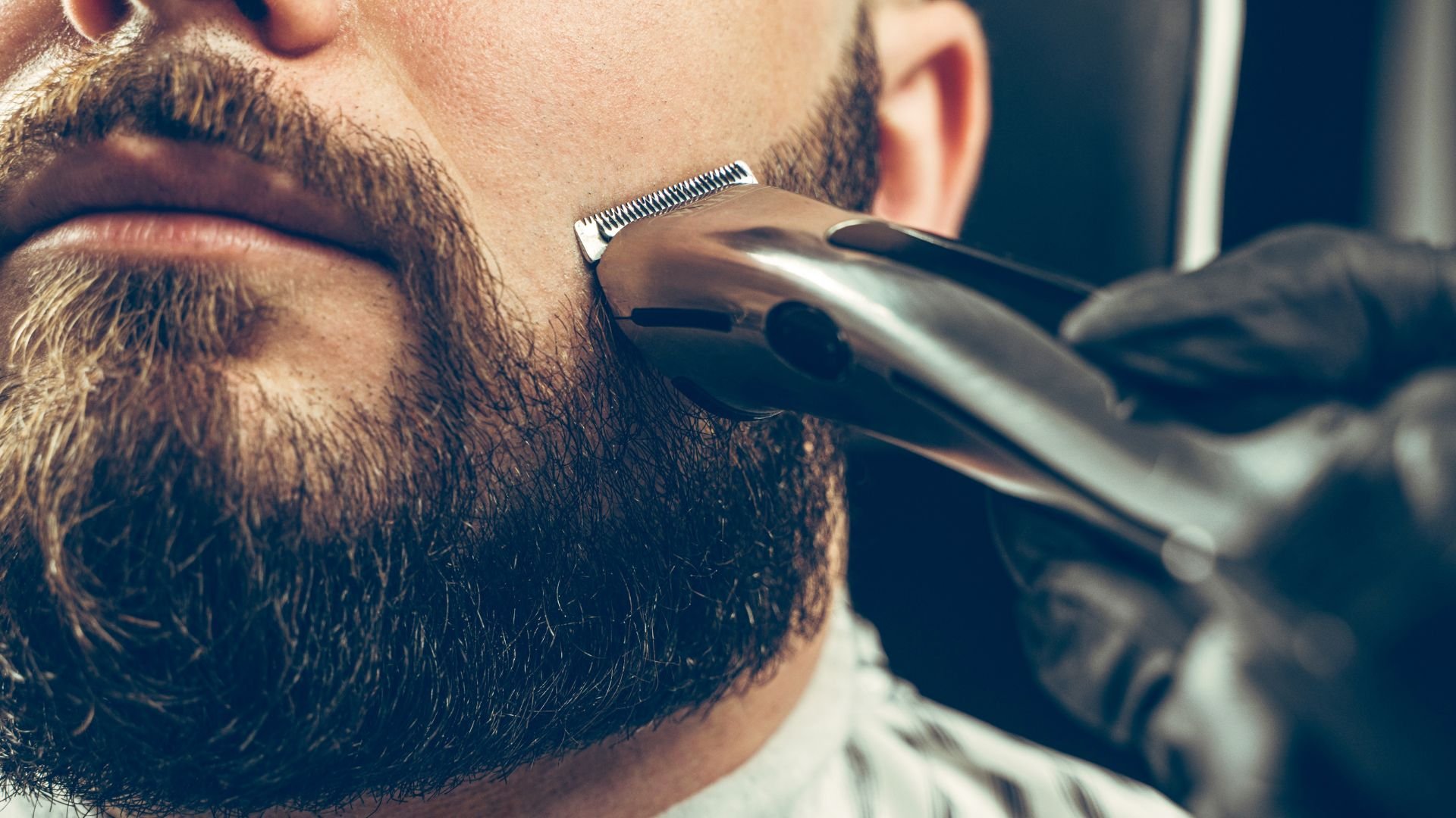 Close-up of electric trimmer grooming a thick beard in barbershop