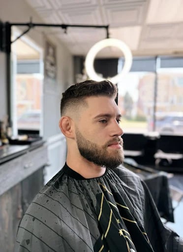 Man with short haircut and beard sits in barbershop chair near ring light