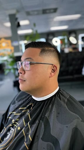 Person getting haircut at barbershop, wearing glasses and black cape