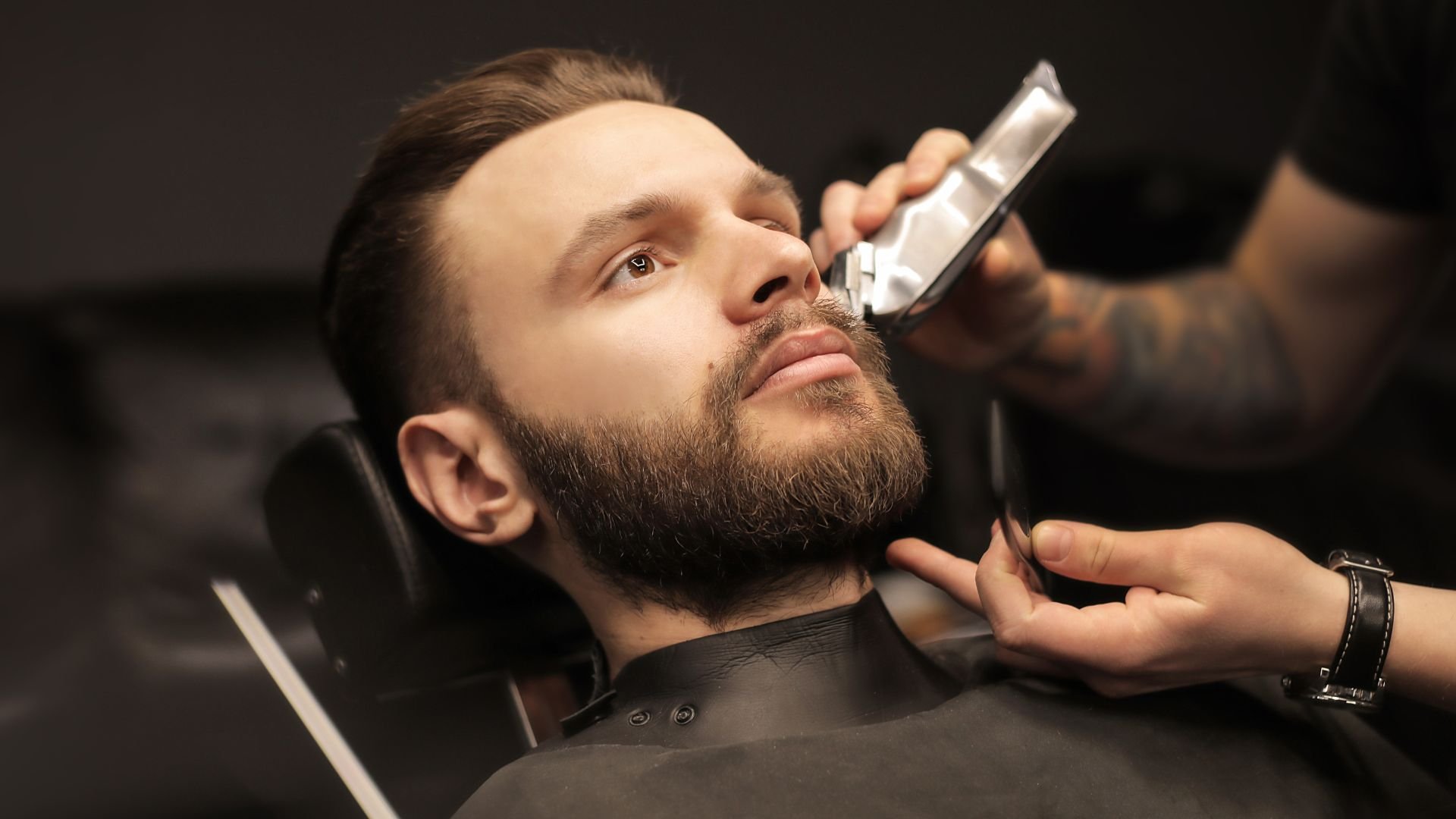 Barber carefully trimming beard of client in professional barbershop
