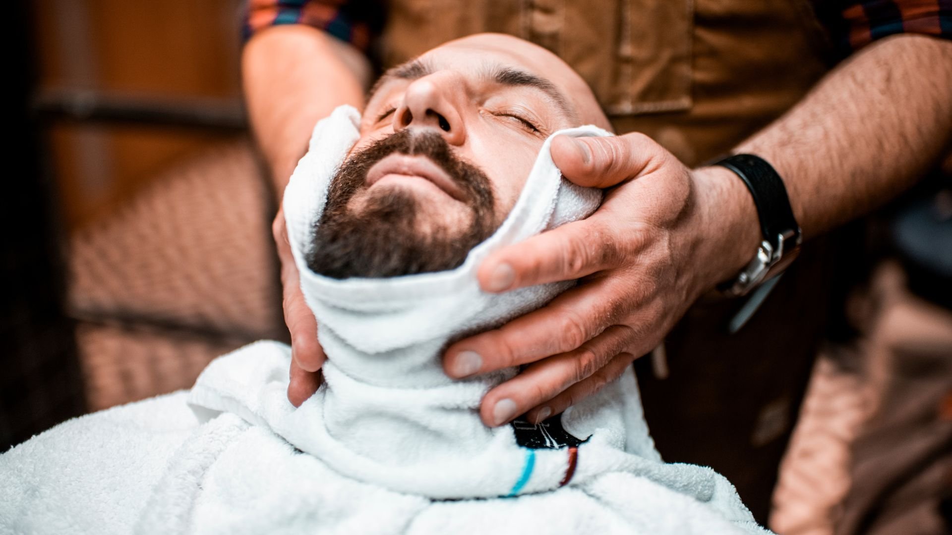 Barber wrapping hot towel around client's face during beard grooming