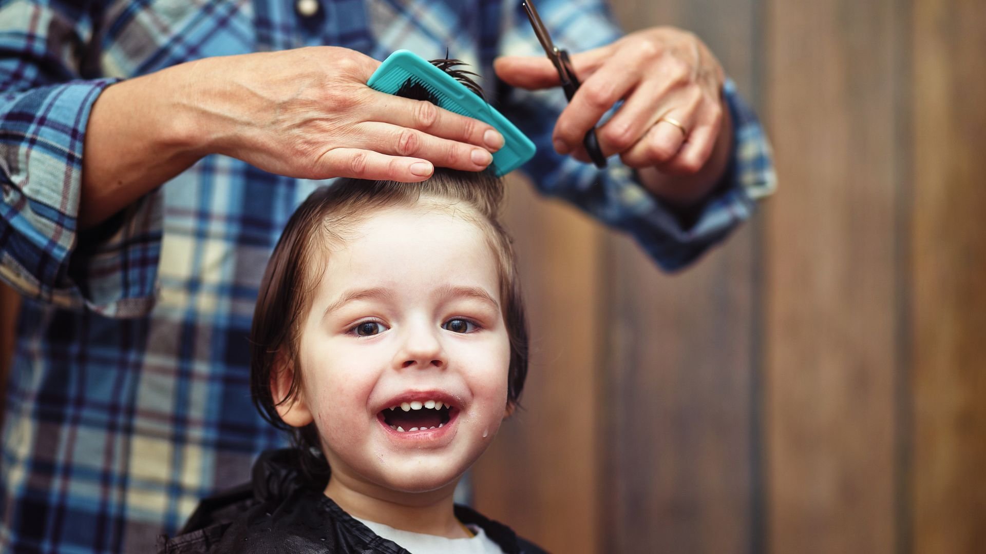 Smiling child getting haircut, hairdresser combing and cutting hair